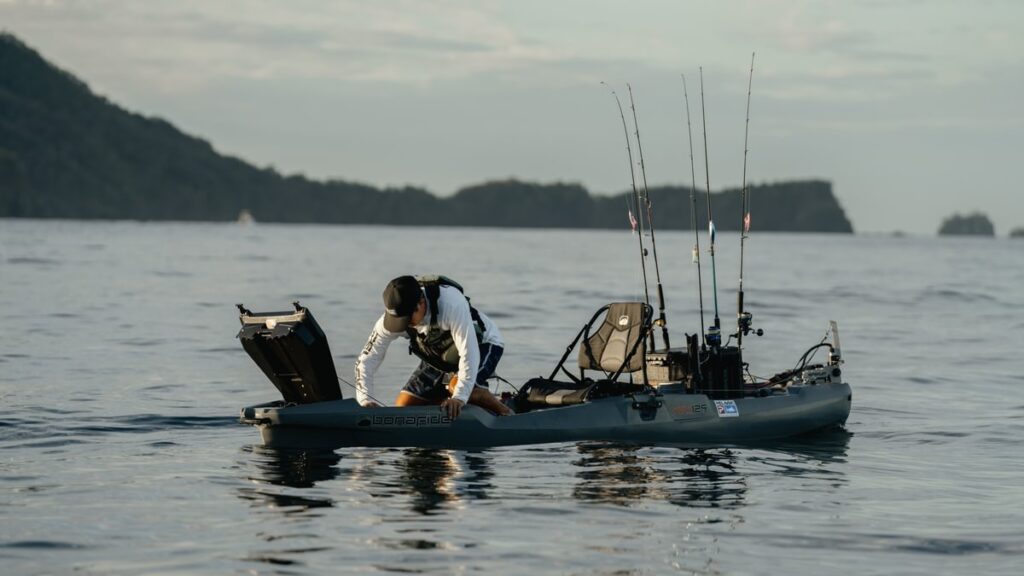 Wędkarz bezpiecznie wyciąga rybę z wody, siedząc na stabilnym kajaku wędkarskim Bonafide PWR 129. Pokaz stabilności markowego kadłuba podczas finałowej fazy holu