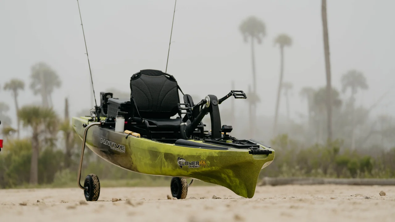 Kajak Native Watercraft Slayer MAX stojący na piaszczystym brzegu na opuszczonych kołach zintegrowanego wózka SideKick Wheel Transport System