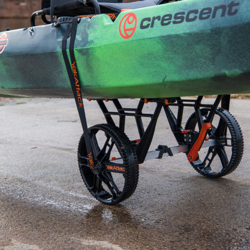 Zielony kajak Crescent zamocowany pasem na wózku transportowym YakAttack TowNStow Bunkster Kayak Cart na utwardzonym nabrzeżu