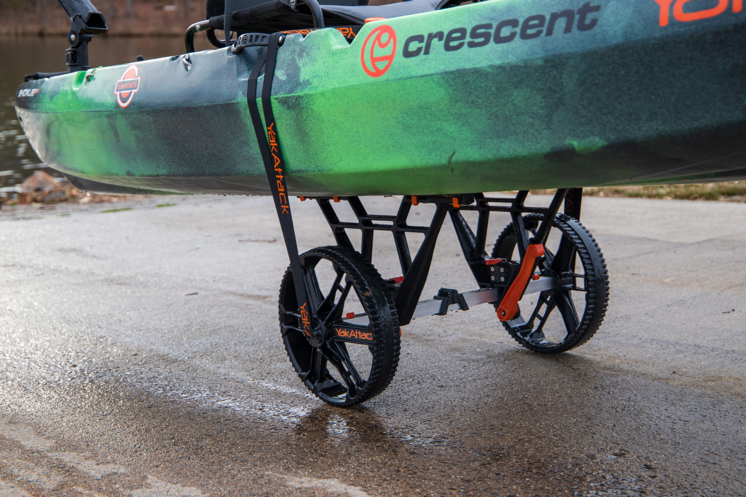 Zielony kajak Crescent zamocowany pasem na wózku transportowym YakAttack TowNStow Bunkster Kayak Cart na utwardzonym nabrzeżu