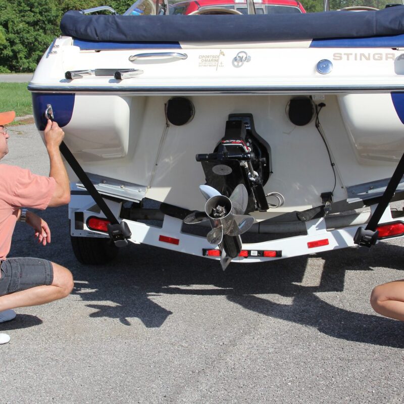 Nierdzewny pas transportowy BoatBuckle SS zamontowany na ramie przyczepy, zabezpieczający pawęż łodzi motorowej.