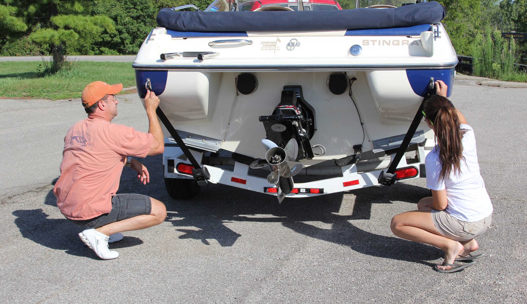 Nierdzewny pas transportowy BoatBuckle SS zamontowany na ramie przyczepy, zabezpieczający pawęż łodzi motorowej.