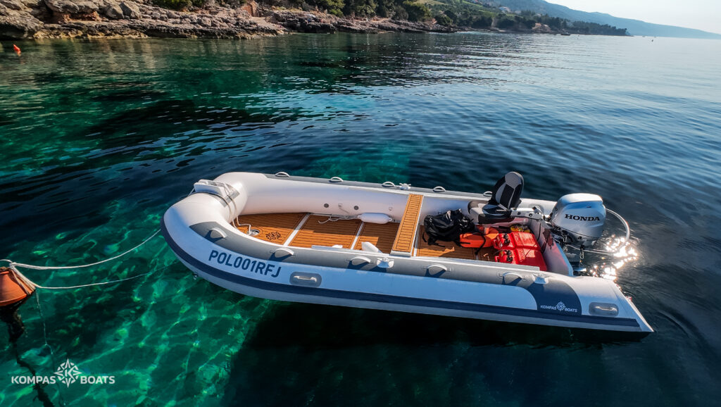 Turystyczny ponton Kompas Boats Croatia 490 przygotowany do wodowania. Widoczne pancerne dno z wojskowego PVC o grubości 1,6 mm, ułatwiające wchodzenie stopnie na pływakach oraz elegancki pokład pokryty antypoślizgową matą EVA.